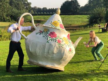 Twee mensen voor een levensgrote theepot op een weiland