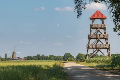 Houten uitkijktoren bij een veld en met een malen op de achtergrond