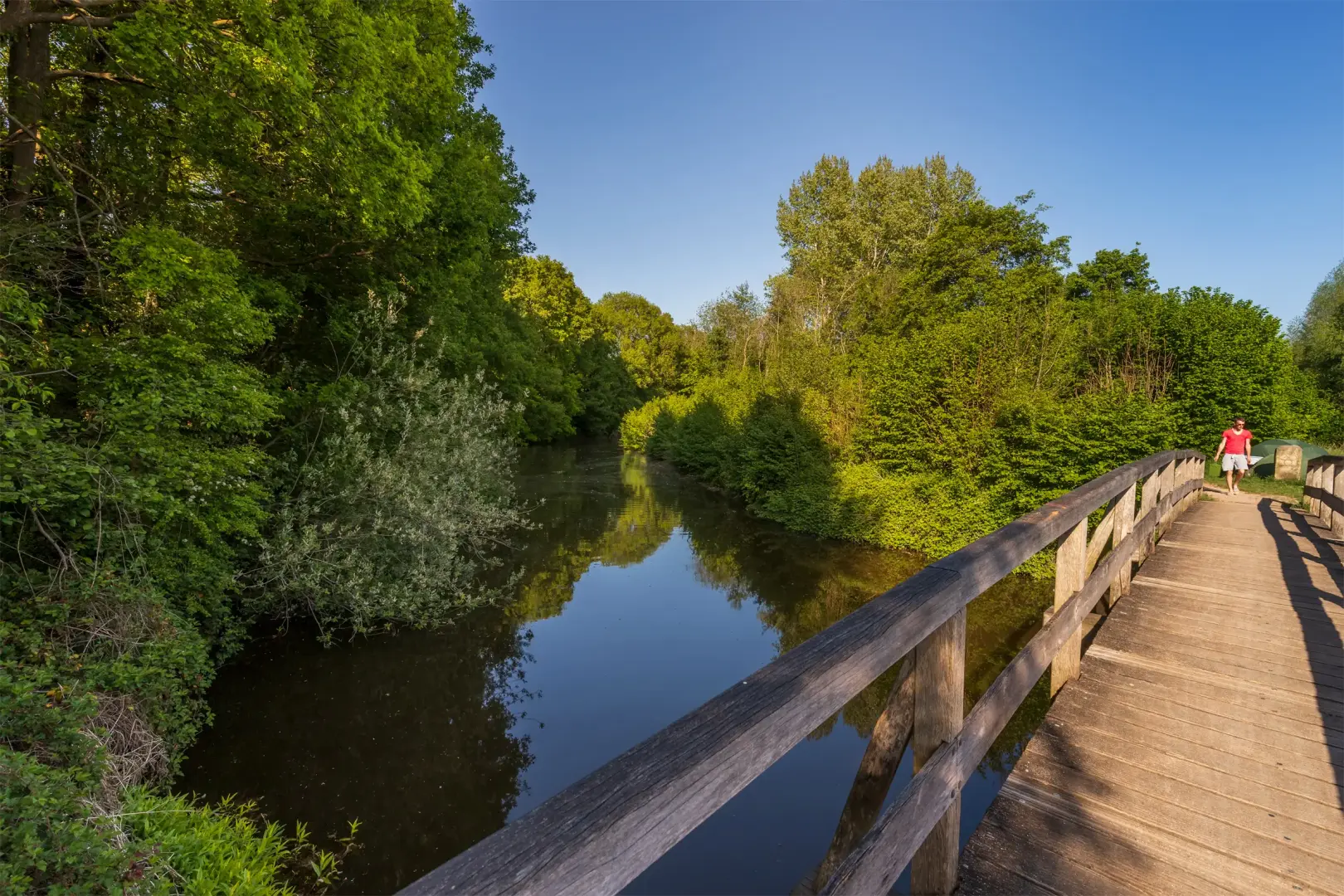 Riviertje bij een houten brug voor wandelaars en met bomen er om heen